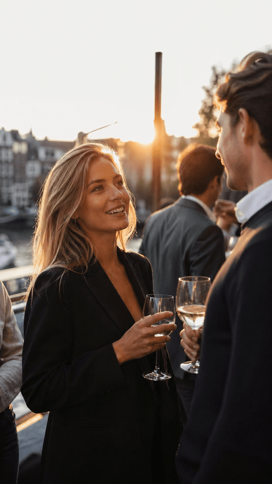 Borrel langs een Amsterdamse gracht bij zonsondergang, gasten in gesprek met een glas wijn